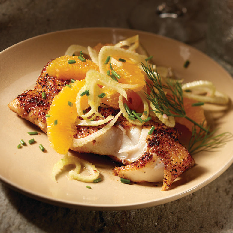 Plated dish of fish with citrus and noodles on a textured surface