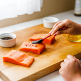Person seasoning salmon fillets on a wooden cutting board with a brush.