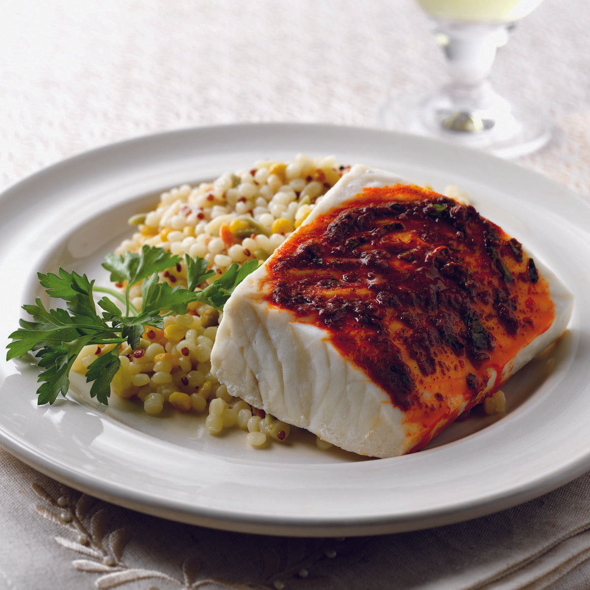 Plated dish of grilled halibut with couscous on a white plate, accompanied by a glass of white wine.