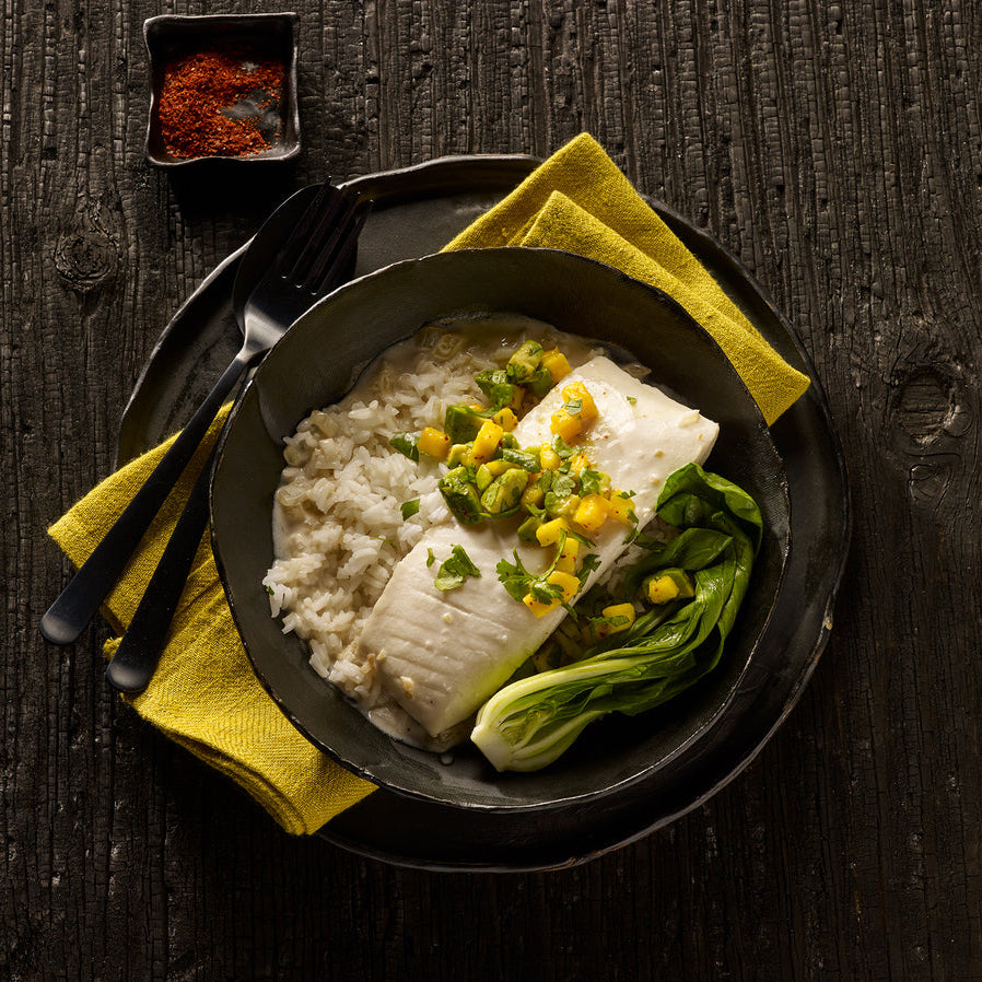 Plated dish of halibut with rice, mango salsa, and vegetables on a dark wooden surface